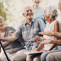 Vier Senioren lachen zusammen, eine Pflegerin ist im Hintergrund zu sehen