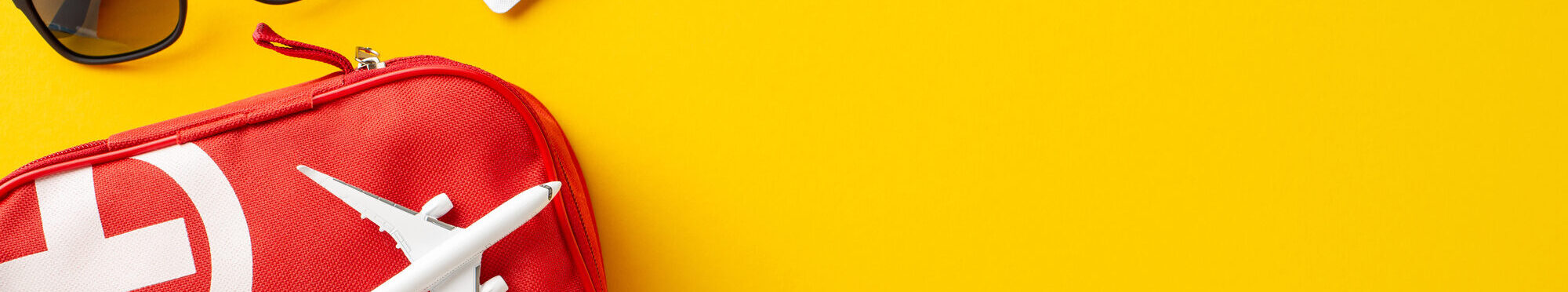 Travel safety essentials arranged with a red first aid kit, airplane, and passport against a vibrant yellow backdrop. Highlights health preparation for trips