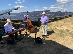 Das Foto zeigt drei Männer, die vor den Sonnenmodulen Musik machen.