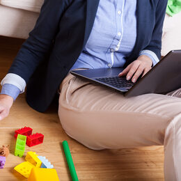 Eine Frau arbeitet am Computer. Neben ihr liegt Spielzeug auf dem Boden.