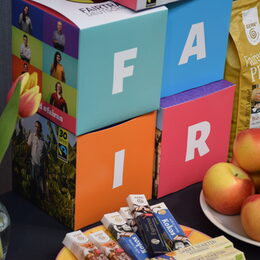 Boxen mit der Aufschrift "FAIR" und Fairtrade-Produkte wie Schokolade, Äpfel und Kaffee