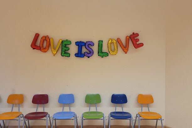 Buchstabenballons mit dem Schriftzug Love is Love an einer Wand über einer bunten Stuhlreihe