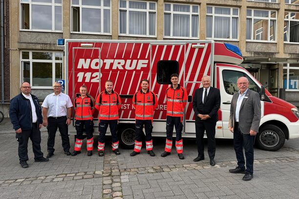 Gruppenbild mit Azubis und Verantwortlichen vor einem Rettungswagen