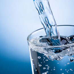 Pouring water into glass on blue background