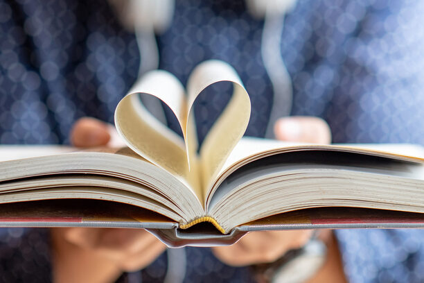 Book lover or love reading concepts. Male hand holding book with heart shape page folded.