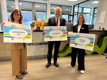 Gruppenbild zu Familienkommune. Vertreter halten Schilder im Familienbüro hoch.