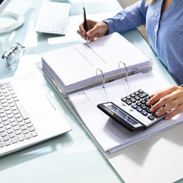 Businesswoman's Hand Calculating Bill In Office