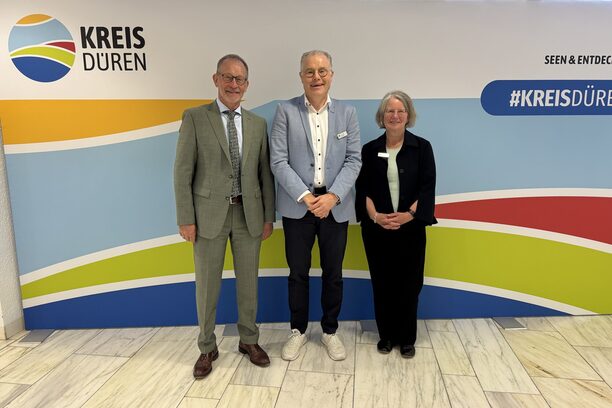 Das Bild zeigt zwei Männer und eine Frau vor einer Stellwand des Kreises Düren