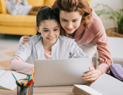 Eine Mutter und Ihre Tochter sitzen lächelnd vor einem PC.